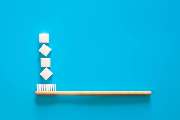Natural eco-friendly bamboo toothbrush with sugar cubes on a blue background, flat lay. - Fotó, kép