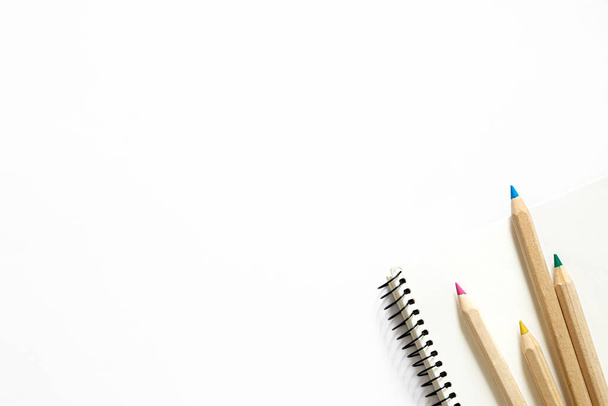 Wooden pencils of different colors and a notebook on a white background, top view, copy space. - Foto, Imagem
