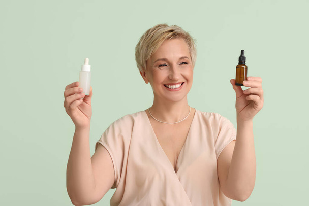 Mature woman with bottles of serum on green background - Foto, immagini