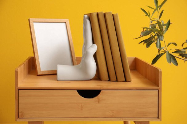 Stylish bookend and blank frame on table near yellow wall - Photo, Image