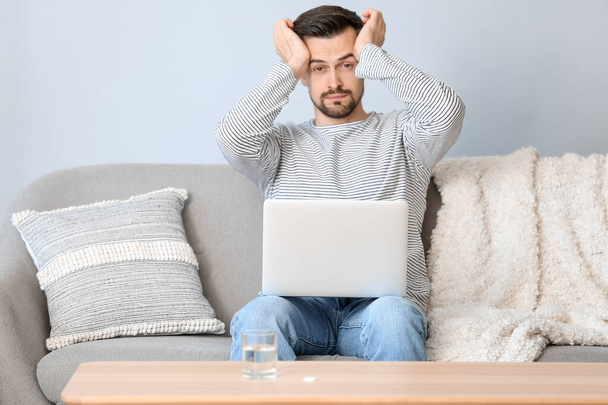 Jeune homme avec ordinateur portable souffrant de maux de tête à la maison - Photo, image