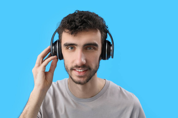 Mladý brunetka muž ve sluchátkách na modrém pozadí, detailní záběr - Fotografie, Obrázek