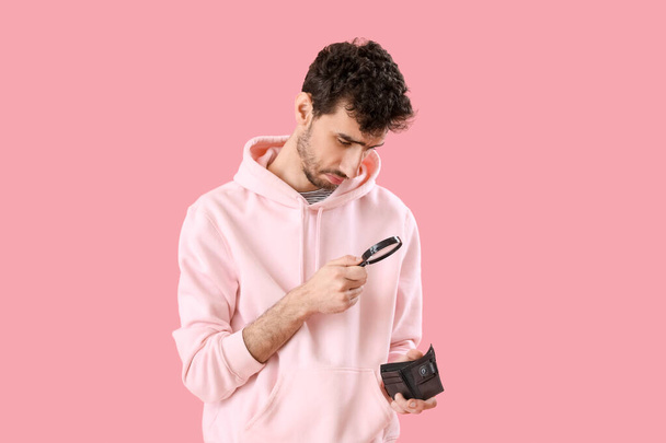 Young man with magnifier and empty wallet on pink background - Фото, изображение