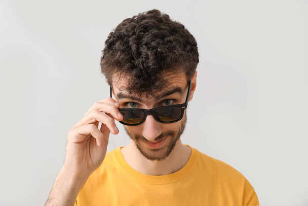 Молодой брюнетка мужчина в солнечных очках на светлом фоне, крупным планом - Фото, изображение
