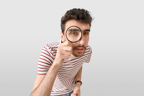 Young man looking through magnifier on light background, closeup - Photo, Image