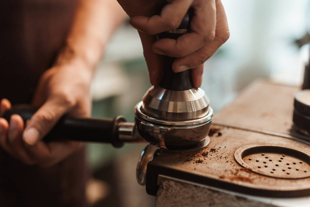 Closeup hand of barista preparation tampering ground coffee in portafilter for espresso machine. Coffee making concept. - Photo, Image
