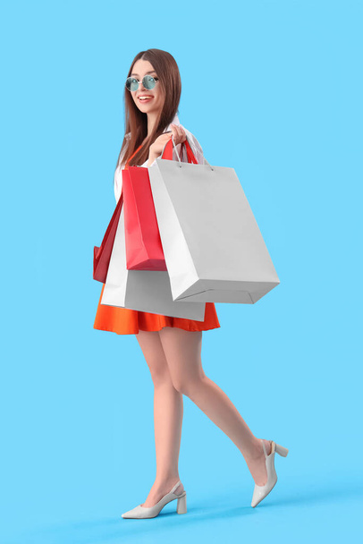 Mladá žena s nákupními taškami na modrém pozadí - Fotografie, Obrázek