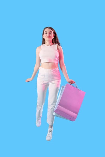 Young woman with shopping bags jumping on blue background - Foto, Bild