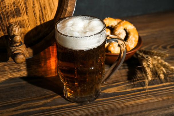 Mug of cold beer and wooden barrel on table. Oktoberfest celebration - Foto, Imagen