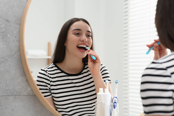 Young woman brushing her teeth with plastic toothbrush near mirror in bathroom - Photo, Image
