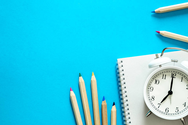Cuaderno, lápices y un reloj despertador sobre fondo azul, vista superior, espacio para copiar, concepto escolar. - Foto, imagen