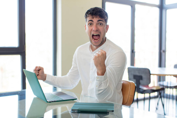 young handsome man feeling shocked,laughing and celebrating success. working at home concept - 写真・画像