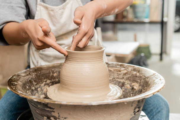 湿った粘土から花瓶を作るエプロンの若い女性職人の作物のビューとぼやけたセラミックワークショップで回転陶器ホイールで作業,陶器の作成プロセス - 写真・画像