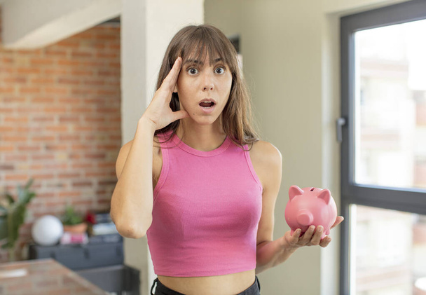 young pretty woman looking happy, astonished and surprised piggy bank concept - Foto, imagen