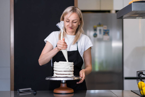 Kohdennettu ruoka bloggaaja osoittaa prosessi tehdä kermainen kotitekoinen kakku seuraajille sosiaalisen median blondi nainen esiliina laittaa valkoinen mastiksi paistettu taikina leivonnaiset kartio - Valokuva, kuva