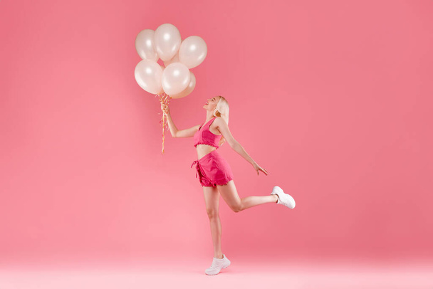 Full length shot of romantic lovely blonde lady holding baloons want to fly up, posing isolated on pink color background, studio, side view, free space - Photo, Image