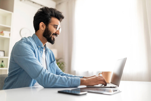 Mosolygó indiai férfi író Laptop használata közben dolgozik otthon Office, Boldog fiatal húsvéti Freelancer Guy Ül az asztalnál, és gépelés billentyűzeten, Kommunikáció Online, Írás Email, Másolás tér - Fotó, kép