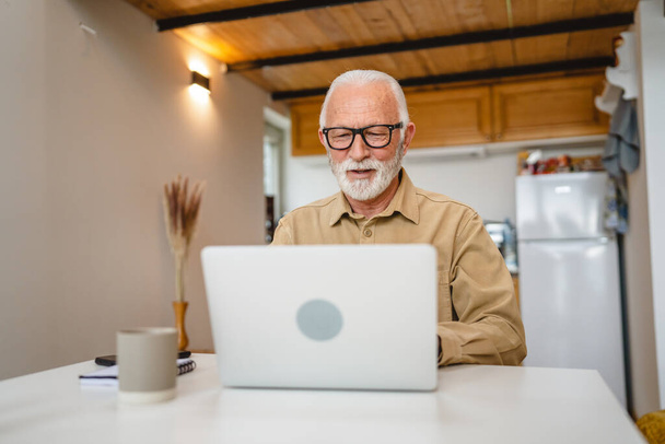 One senior caucasian man grandfather with beard and eyeglasses work on laptop use computer at home - 写真・画像