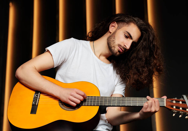 Zenei tehetség. Fiatal latin srác tanul játszani akusztikus gitár ül a fekete háttér, rögzíti a dalt a szakmai stúdióban. Diák zenész pózol a hangszerével. - Fotó, kép