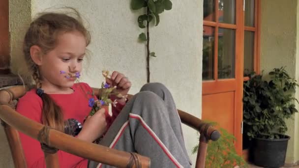 Mała dziewczynka na krześle z bukietem kwiatów. Samotność dziecka Depresyjny nastrój - Materiał filmowy, wideo