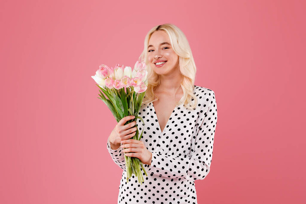 Portret szczęśliwej europejskiej damy cieszącej się aromatycznym bukietem kwiatów, urodziny, pozowanie izolowane na różowym tle studio. Świętowanie wakacji, mody, stylu życia, reklamy i oferty - Zdjęcie, obraz