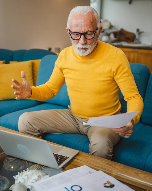 Un anziano uomo caucasico nonno con barba e occhiali lavora sul computer portatile utilizzare a casa risolvere il problema preoccupato frustrazione - Foto, immagini