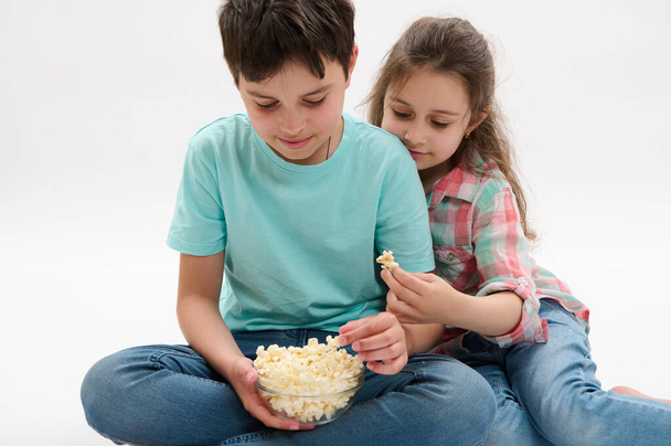 Bambini adorabili, ragazzo adolescente e bambina, fratello e sorella che mangiano popcorn, si divertono insieme, su uno sfondo isolato di studio bianco. Svaghi di famiglia. Gente. Bambini. Intrattenimento, Cibo e bevande - Foto, immagini