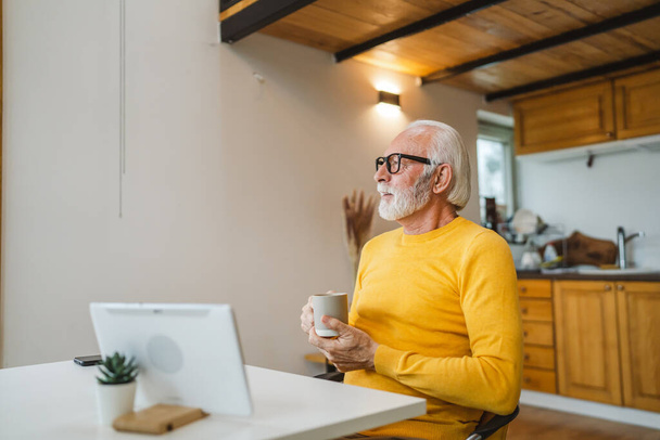 Один старший чоловік сидить вдома на кухні з чашкою чаю або кави, приймаючи гальма від роботи або готуючись до щоденного завдання ранкового звичайного справжнього чоловіка копіювати простір домашнього життя активного старшого
 - Фото, зображення