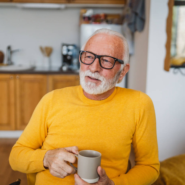 One senior man sit at home in the kitchen with cup of tea or coffee taking a brake from work or prepare for daily task morning routine real person copy space domestic life active senior - Photo, Image