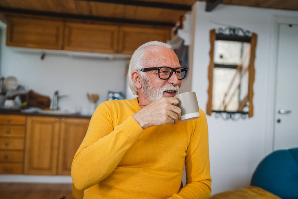 Один старший чоловік сидить вдома на кухні з чашкою чаю або кави, приймаючи гальма від роботи або готуючись до щоденного завдання ранкового звичайного справжнього чоловіка копіювати простір домашнього життя активного старшого
 - Фото, зображення