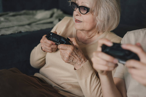 Yukardan, gündelik giysiler ve gözlüklü genç sarışın kadın koltukta oturuyor ve evde vakit geçirirken video oyunu oynuyor. - Fotoğraf, Görsel