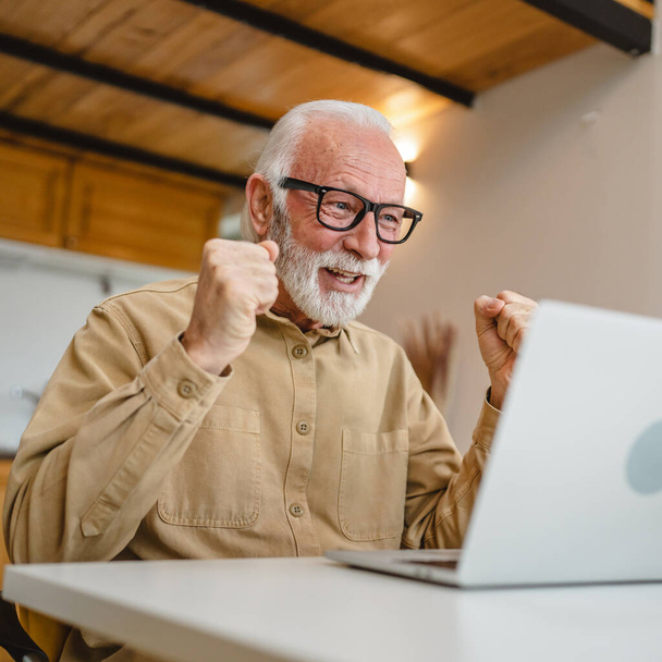 ひげと眼鏡の仕事を持つ1つのシニア白人男性祖父ノートパソコン上で使用コンピュータで自宅オンライン幸せな笑顔の成功 - 写真・画像