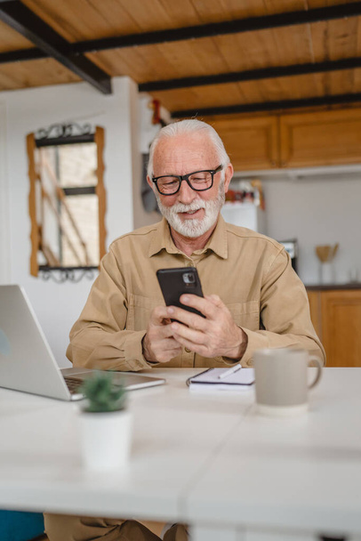 One man senior caucasian male with gray beard sit in day use mobile smart phone to make a call talk copy space work from home - Foto, afbeelding