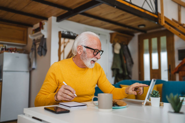 Jeden starszy biały mężczyzna dziadek z brodą i okularami pracować na tablecie cyfrowym używać komputera w domu szczęśliwy uśmiech sukces - Zdjęcie, obraz
