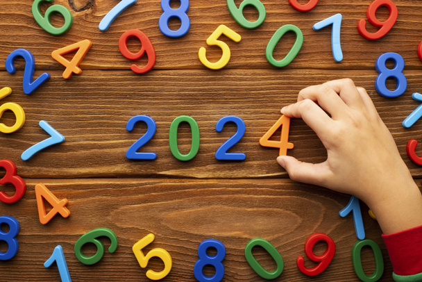 Feliz año nuevo 2024 fondo. Una mano de niño pliega números de plástico en el número del nuevo año 2024 - Foto, imagen