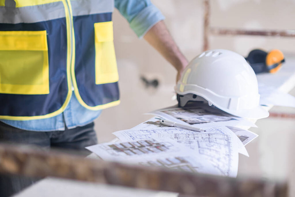 Travailleur en uniforme professionnel mettant le casque sur tas de documents de projet équipement de construction et règles de sécurité pendant le processus de rénovation sur place - Photo, image