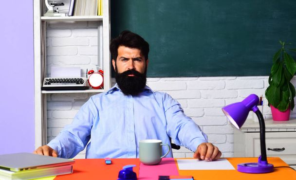 Serious bearded male teacher in classroom. Learning and education. Teachers day. Professional teacher or university professor sitting at table with laptop in auditory. Student studying in university - Photo, Image