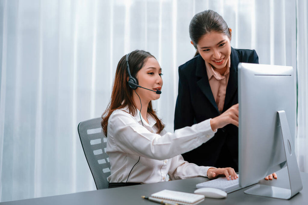 Asian female customer support operator wearing headset is guided by her supportive manager. Experienced colleague help operator handle a call with a client, providing advice and guidance. Enthusiastic - Фото, изображение