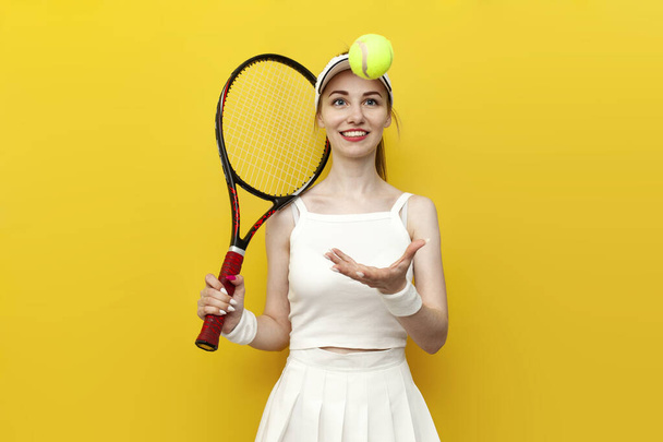 girl tennis player in sportswear holding tennis racket and ball on yellow isolated background and smiling, portrait of female tennis coach in white uniform with sports equipment - Photo, Image