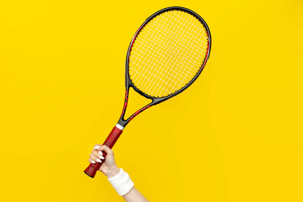 female hand holds tennis racket on a yellow isolated background, sports equipment, close-up - Foto, Imagen