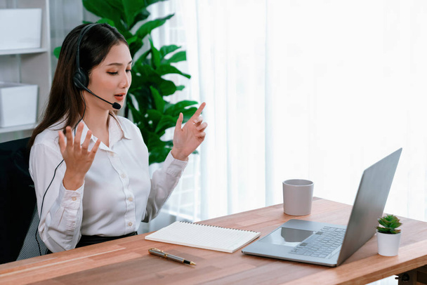 Asian call center with headset and microphone working on her laptop. Female operator provide exceptional customer service. Supportive call center agent helping customer on inquiry. Enthusiastic - Foto, Imagem