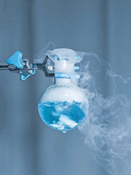 Blue liquid in glass flask with white smoke during experiment in laboratory - Zdjęcie, obraz