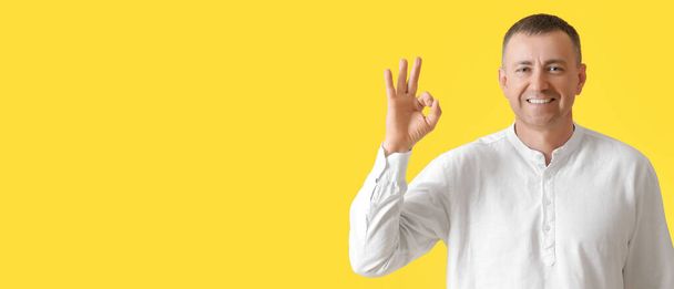 Volwassen man met OK gebaar op gele achtergrond met ruimte voor tekst - Foto, afbeelding