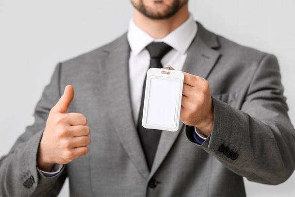 Young businessman with blank badge showing thumb-up on light background, closeup - Foto, Bild