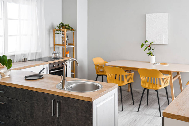Интерьер светлой кухни со столом и раковиной на деревянной столешнице - Фото, изображение