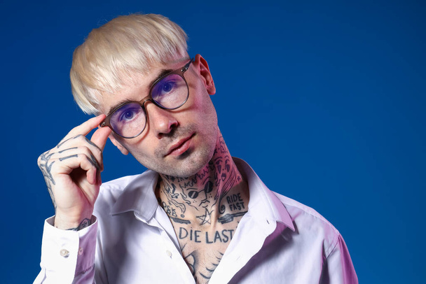 Young tattooed man in eyeglasses on blue background, closeup - Photo, Image