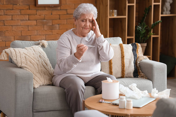 Μια ηλικιωμένη γυναίκα με θερμόμετρο στο σπίτι. - Φωτογραφία, εικόνα