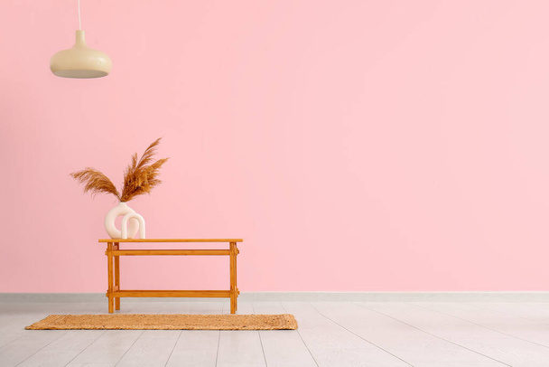 Houten tafel met pampas gras in vaas bij roze muur - Foto, afbeelding