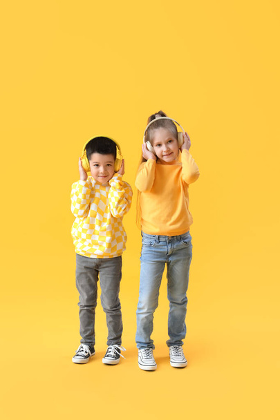 Cute little children in headphones and sweaters on yellow background - 写真・画像