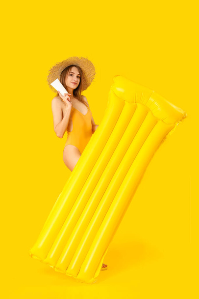 Young woman with sunscreen cream and inflatable mattress on yellow background - Photo, Image